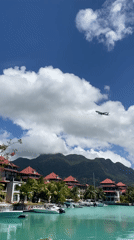 Plane flies over turquoise waters and red-roofed Seychelles shoreline