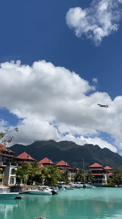 Plane flies over turquoise waters and red-roofed Seychelles shoreline