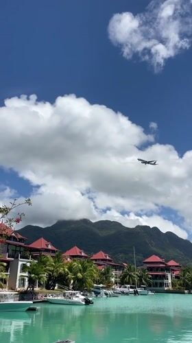 Plane flies over turquoise waters and red-roofed Seychelles shoreline