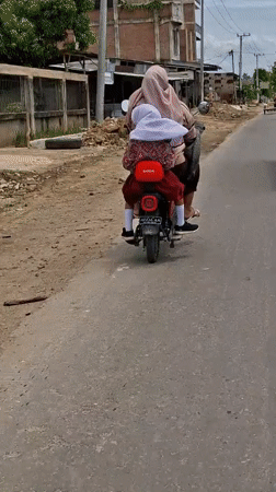 Woman and child ride electric scooter in Indonesian residential area