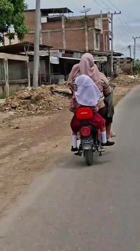 Woman and child ride electric scooter in Indonesian residential area
