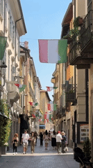 Italian flags decorate narrow Como street as pedestrians pass