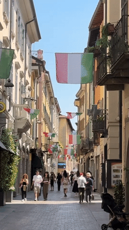 Italian flags decorate narrow Como street as pedestrians pass