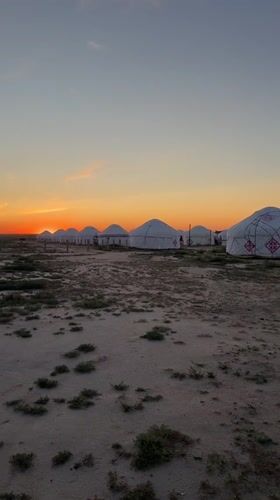 Yurts on sandy plains and a calm waterside sunset.