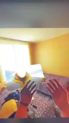 Here is a description of the video.

The video shows a person lying on a bed covered with a star-patterned blanket. They are watching an animated video on a screen that is positioned between them and the camera, and the light coming from the window is reflecting off the screen. The animated video features a character with blond hair and a gold-trimmed outfit. The person in the video uses a gloved hand to navigate the interface on the screen. A yellow bag rests beside them on the bed. The room's walls are yellow, and the window behind the screen has blinds. The video is likely shot from a phone.