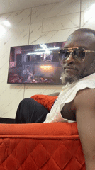 Man in sunglasses watches TV on red couch in Nigeria