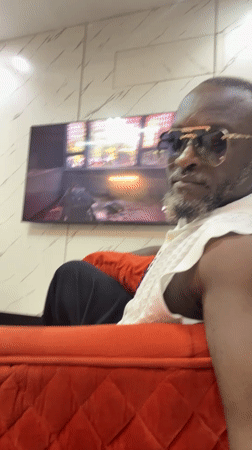 Man in sunglasses watches TV on red couch in Nigeria