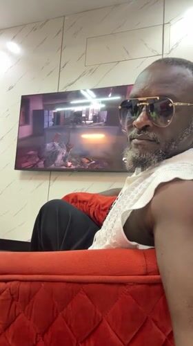 Man in sunglasses watches TV on red couch in Nigeria