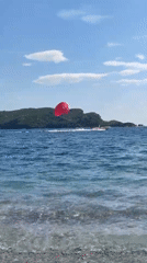 Beachgoers enjoy parasailing and swimming during clear afternoon