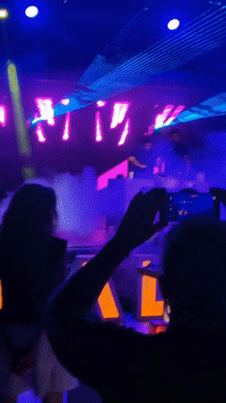 Two DJs perform at a lively nightclub event under colorful lights