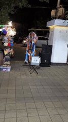 Street performer in feathered regalia plays music on Sochi sidewalk