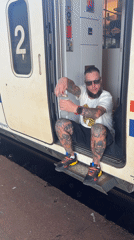 Tattooed passenger waits in train doorway at Mostar station