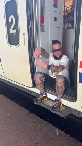 Tattooed passenger waits in train doorway at Mostar station