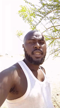 Man in white tank top observed in sandy Nigerian environment