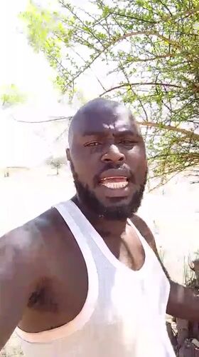 Man in white tank top observed in sandy Nigerian environment