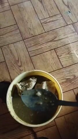 Here is a concise description of the video:

The video shows a child sitting on a wood-patterned floor. They are reaching towards a purple bowl filled with what appears to be food. Later, the camera focuses on a close-up of a yellow container filled with a dark liquid and some solid food items. A person is shown using a spoon to move the food around in the container. The context and nature of the food are unclear.