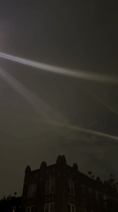 Light beams streak across New York sky above brick buildings