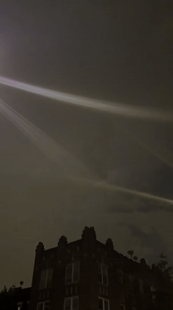 Light beams streak across New York sky above brick buildings
