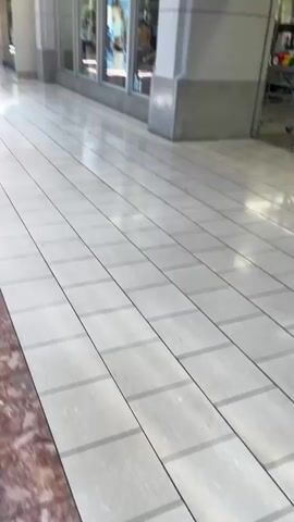 The video shows the exterior of an Old Navy store. The store entrance is visible, with clothing racks and mannequins displayed inside. A shopping cart is parked near the entrance. The floor is tiled, and a portion of the wall is made of light-colored stone. A sign advertising a sale is hanging above the entrance.