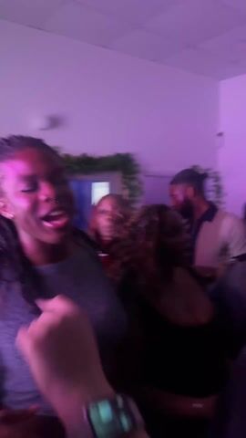 The video shows a dimly lit indoor setting with pink and blue lighting, possibly a party. Individuals are present, though mostly blurred. A person holds a red cup filled with a pink liquid. The camera movement is unsteady. There appears to be a phone in the background. It’s difficult to discern much detail due to the blurriness.