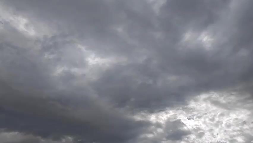 This is a video of a cloudy sky. The clouds are a mix of grays and whites, with some hints of blue sky peeking through in a few places. The clouds appear to be moving, suggesting that there is some wind. The lighting suggests it is daytime, but the heavy cloud cover makes it difficult to determine the exact time. There are no people, objects, or any other discernible features in the video, only the sky and clouds. The scene is very atmospheric and somewhat dramatic due to the dark, heavy clouds.