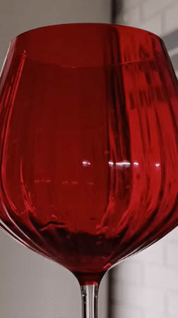 Person fills red glass, holds colorful eggs in kitchen