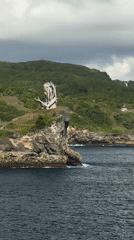 Tourist photographs clifftop statue at Nusa Penida coastal viewpoint