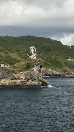 Tourist photographs clifftop statue at Nusa Penida coastal viewpoint