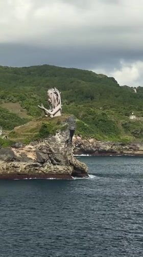 Tourist photographs clifftop statue at Nusa Penida coastal viewpoint