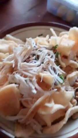 The video shows a close-up of a dish containing white shredded meat, possibly chicken, and what appear to be pieces of fried food or crackers. There are also some green flecks, likely herbs. The food is presented on a plate. The initial shot is slightly blurred, but it quickly comes into focus.