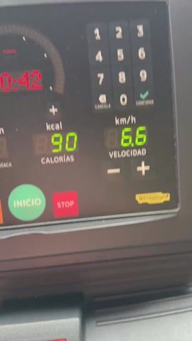 The video shows a person using a treadmill in a building with a view of a harbor. The treadmill's display indicates a time of 20:49, 90 calories burned, and a speed of 6.6 km/h. Through the window, multiple ships are docked in the harbor, and a city skyline is visible in the background. The camera pans slightly to show more of the harbor view.