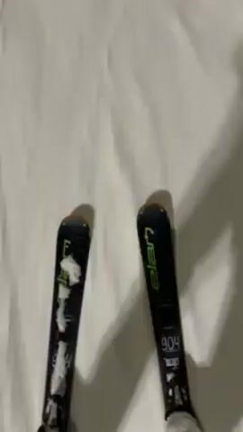 Here is a description of the video:
The video shows a first-person perspective of someone skiing down a snowy slope at night. The skier is using black skis with "Elan" written on them. The slope is illuminated by bright lights, and there are a few other skiers visible in the distance. It appears to be snowing lightly. The ground is mostly white, with visible ski tracks.
