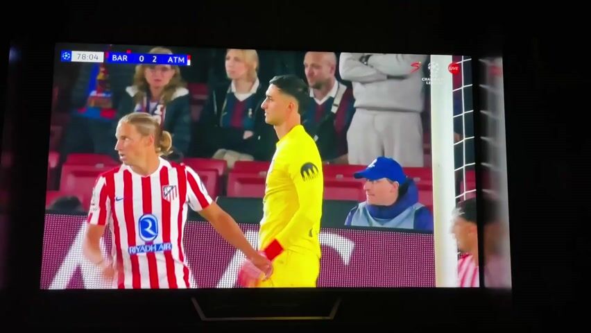 The video shows a soccer game on TV. The score is Barcelona 0 and Atletico Madrid 2. A player in a blue and red jersey is dribbling the ball. A player in a red and white striped jersey slides to try to take the ball away from him, but the ball goes over the sliding player and the other player is able to maintain possession. There are a few other players on the field. The game is being televised live on Supersport, which is the broadcast signal at the top right of the screen.