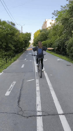 Arms-out bicycle ride along a sunny city bike path