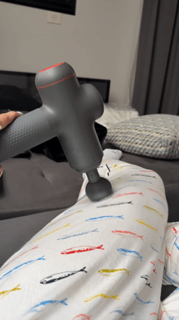 Person uses massage gun during late-night self-care session