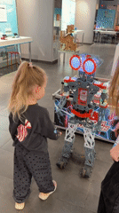Child encounters illuminated metal robot with circular eyes
