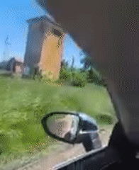 Driver travels rural dirt road past field structure
