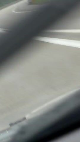 A white pickup truck drives on a highway under a cloudy sky. The truck is in the right lane and appears to be traveling at a moderate speed. Trees line the side of the road, and a highway sign is visible on the left. The highway curves to the right.
