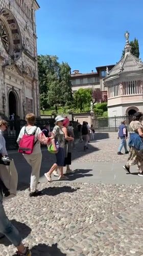 Tourists explore historic Bergamo square on sunny morning