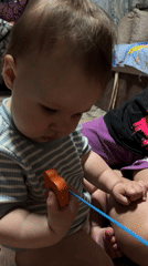 Baby plays with orange toy while showing signs of distress