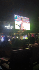 Patrons watch football match on outdoor screen in Offatedo