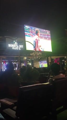 Patrons watch football match on outdoor screen in Offatedo