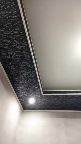 The video shows a close-up view of a modern ceiling with a textured black band along the edges. The ceiling is illuminated by recessed lights. The camera slowly pans across the ceiling, showing the detail of the textured pattern and the clean lines of the ceiling design. The walls below the ceiling are a plain, light color and appear to be unfinished. The overall impression is one of contemporary interior design.