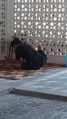A person in black clothing is lying on a rug, using a cell phone. The background features a white patterned wall and a tiled floor.
