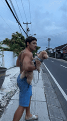 Tattooed man carries small dog on North Kuta sidewalk