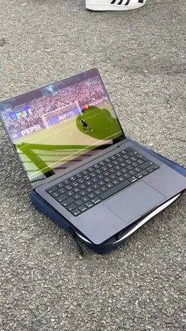 Here is a description of the video.

The video shows a soccer game being played on a laptop on the ground. The laptop is in a case, and the game is being watched by a group of young men sitting nearby. The men are dressed casually and appear to be enjoying the game. There are also bags of snacks and drinks surrounding them. The scene takes place in an outdoor area.