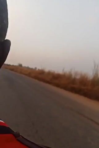 The video depicts a view from a vehicle traveling on an asphalt road. To the right of the road is a field of tall, dry, brown grass. The sky is overcast and appears hazy. The camera seems to be mounted within the vehicle, providing a moving perspective of the roadside.