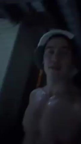A man with a hat and no shirt is standing outside in a snow drift. He is holding a squeaky toy chicken and making it squeak.