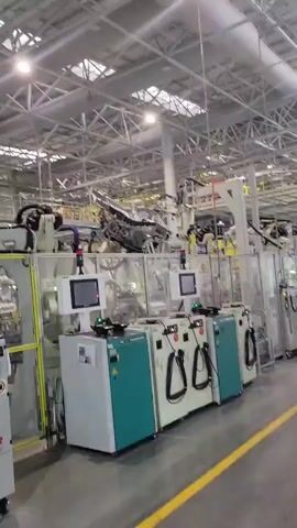 This video captures a view inside a modern, well-lit factory setting in Yufengshan, China. The scene is dominated by industrial machinery, likely an automated assembly line, with a focus on robotic arms and control panels. The ceiling is a complex network of metal beams and pipes, with fluorescent lights providing ample illumination. The floor is a polished concrete surface marked with yellow lines, suggesting a structured operational layout.

The primary subjects are the various pieces of industrial equipment. Several white and teal control units with screens and cables are lined up in the foreground. Behind them, robotic arms are visible, some in motion, suggesting an ongoing manufacturing process. The overall impression is one of advanced technology and automation.

The activity taking place is clearly an industrial manufacturing process. The robotic arms are positioned to perform tasks, and the control panels indicate the operation of sophisticated machinery. There are no people visible in the frame, reinforcing the impression of an automated environment.

Notable details include the clear and bright lighting, suggesting this is likely daytime. The clean and organized appearance of the factory points to a well-maintained facility. A sign visible on one of the machines reads "RF-04". Another visible text on a machine is "TUCKER". The atmosphere is one of efficient operation and technological advancement, devoid of any discernible human emotion. The location is identified as Yufengshan, China.