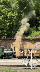 Green steam train departs Pétange station with passengers aboard